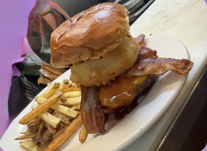 A juicy cheeseburger stacked with bacon and a crispy onion ring, with fries